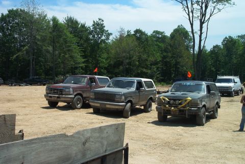 1993 Ford Bronco - Several Ford Broncos and a van are parked on a dirt lot with trees and a blue sky overhead.