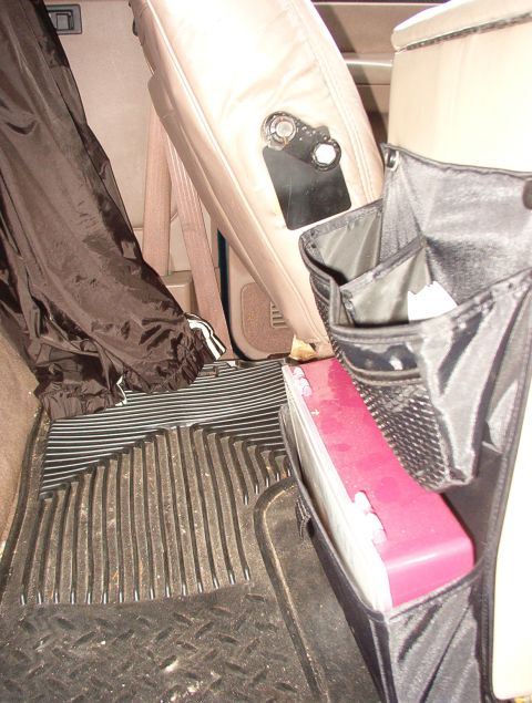 1993 Ford Bronco - The interior of a vehicle shows a seat organizer with a pink item and a black jacket draped over the seat.