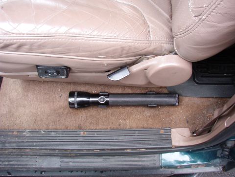 1993 Ford Bronco - A black Maglite flashlight rests on the carpeted floor of a vehicle, near the driver's seat.