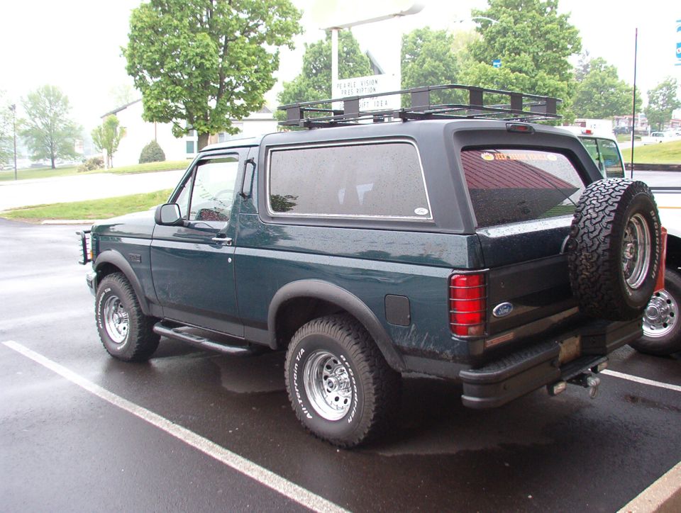 Dark green Ford Bronco rear three-quarter with roof rack and swing-out spare tire