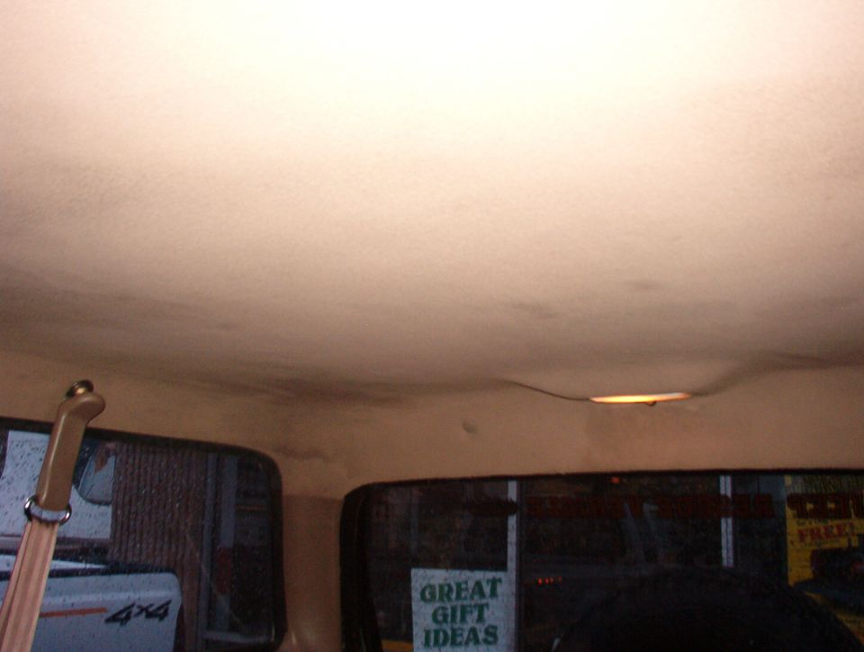 Interior view of a vehicle's headliner and windows. A wooden handle is visible on the left