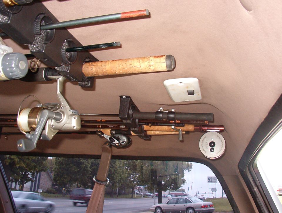 Overhead fishing rod rack mounted to tan headliner inside SUV, road visible outside