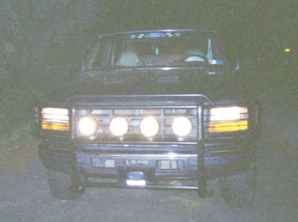 1993 Ford Bronco - Front view of a dark 1992 Ford truck with a grille guard and four illuminated headlights.