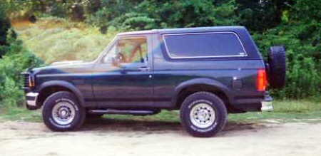 1993 Ford Bronco - A dark green 1993 Ford Bronco is shown from the side, parked outdoors with trees in the background.