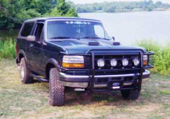 1993 Ford Bronco - A dark green Ford Bronco is parked on a grassy area next to a body of water.