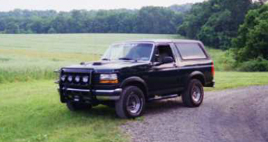 1993 Ford Bronco - This black 1993 Ford Bronco is captured in a three-quarter front view, parked on a gravel road with a scenic rural backdrop.