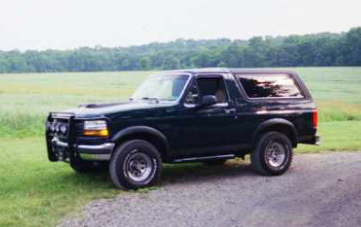 1993 Ford Bronco - 1993 Ford Bronco parked outdoors with a field and trees in the background.