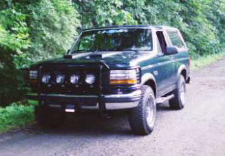 1993 Ford Bronco - A dark green 1992 Ford Bronco is parked on a dirt road with trees in the background.