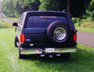 1993 Ford Bronco - Rear view of a 1993 Ford Bronco parked on grass with a paved road in the background.