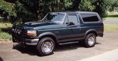 1993 Ford Bronco - This dark green Ford Bronco is shown from a three-quarter front angle, with a bull bar and hood scoop visible.