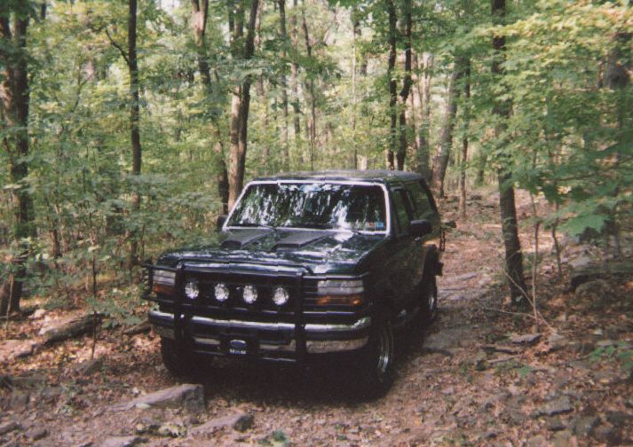 Dark green 1993 Ford Bronco with bull bar and auxiliary lights on wooded trail