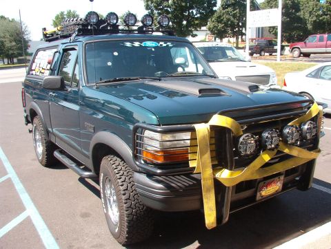 1993 Ford Bronco - A green Ford Bronco is parked in a lot, modified with extra lights and a roof rack.