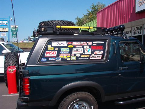 1993 Ford Bronco - This SUV is heavily customized with a roof rack, spare tire, and a collection of decals adorning its rear windows.