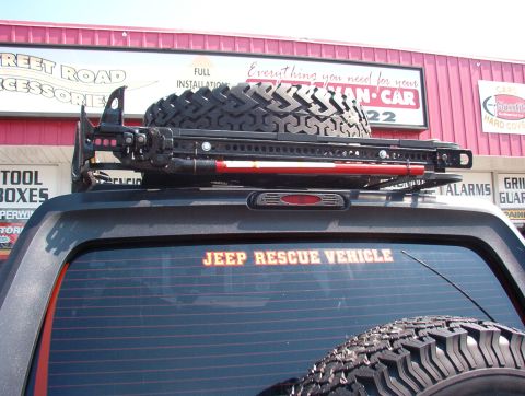1993 Ford Bronco - A Jeep is equipped with a roof rack, spare tire, and a Hi-Lift jack, with a 'JEEP RESCUE VEHICLE' decal on its rear window.