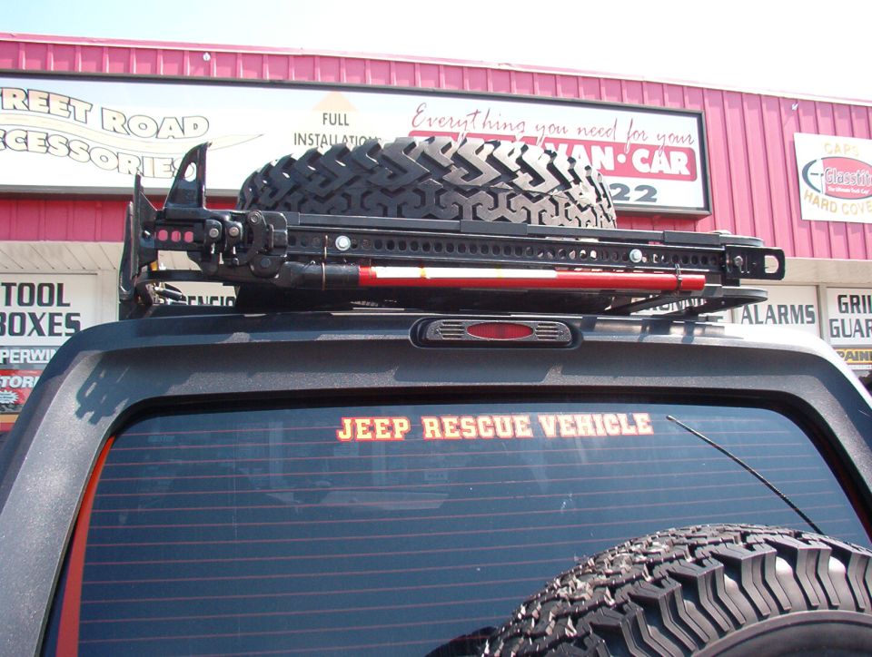 Rear of a Jeep with a roof rack holding a spare tire and a Hi-Lift jack. 'JEEP RESCUE VEHICLE' sticker on the rear window