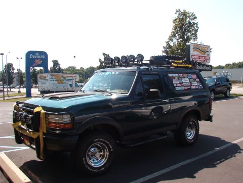 1993 Ford Bronco - A modified Ford Bronco is parked in a lot, adorned with numerous stickers and accessories, with another vehicle visible in the background.