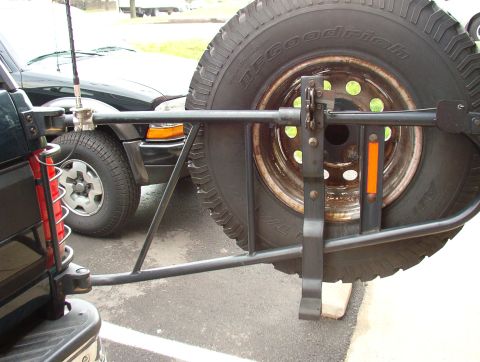 1993 Ford Bronco - A rear-mounted spare tire carrier is visible on a dark SUV, with another vehicle parked behind it.
