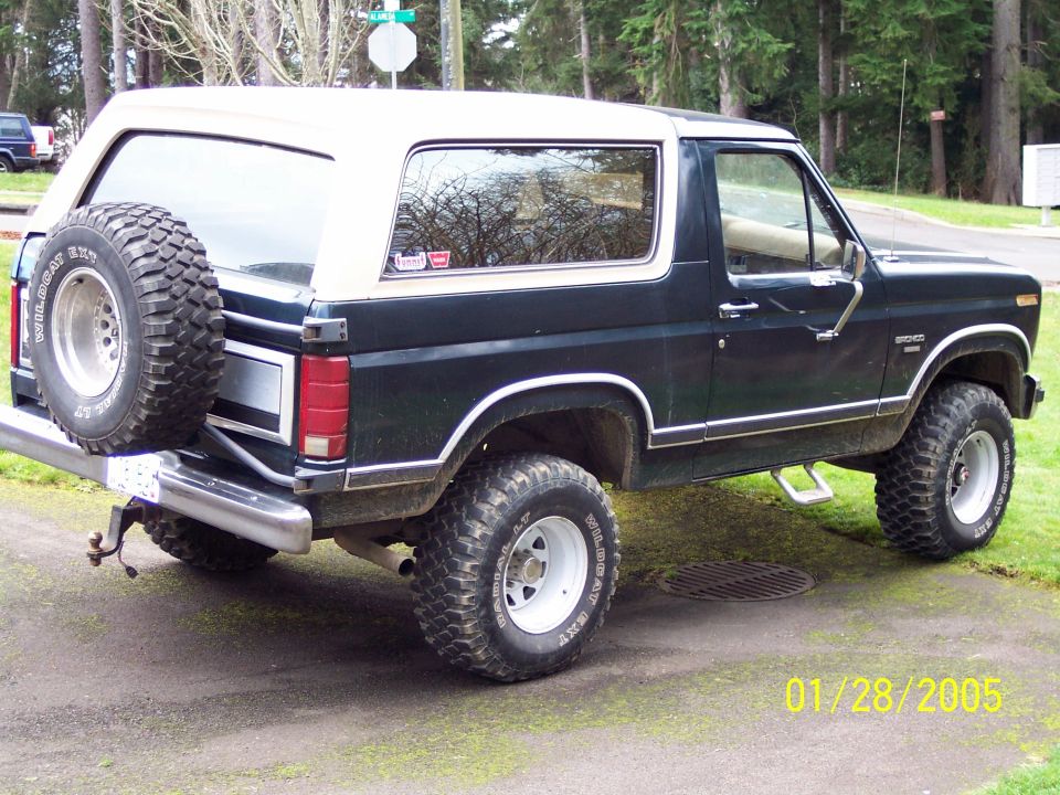 Dark blue Ford Bronco with white top and spare tire on back, lifted suspension