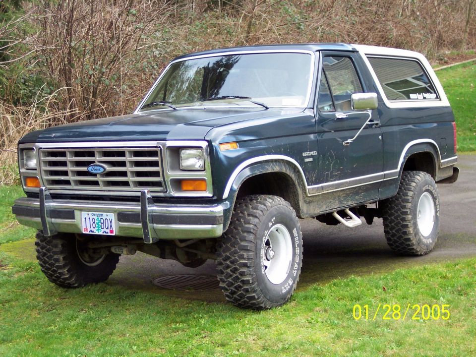 Lifted dark blue Ford Bronco with white camper top, tube bumper and chrome wheels on a driveway
