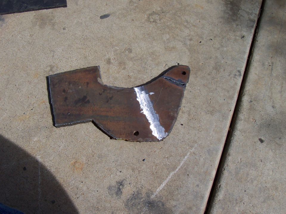 Rusty torch-cut steel bracket plate with ground weld bead on concrete