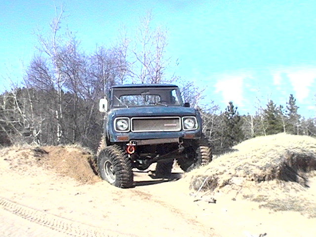 Blue lifted International Scout on big tires cresting a sandy dirt hill, front view