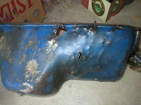 1978 Ford Bronco - This blue oil pan has significant damage, including multiple holes and rust, indicating it is not in usable condition.