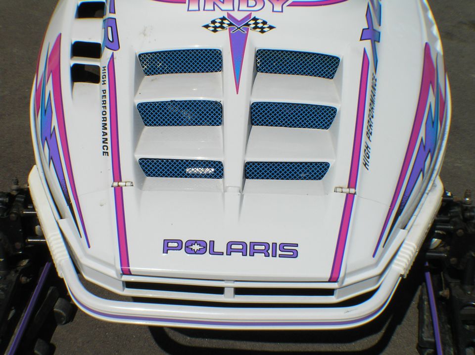 White Polaris Indy snowmobile hood with pink/purple graphics and vents, front view