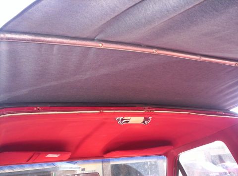 1989 Ford Bronco - The interior ceiling of a vehicle, red upholstery and a grey headliner with a metal support bar.