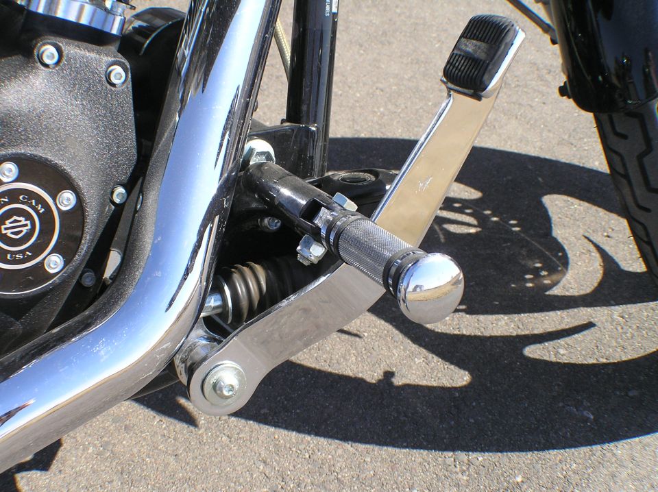 Chrome forward foot control and footpeg on a black Harley-Davidson engine