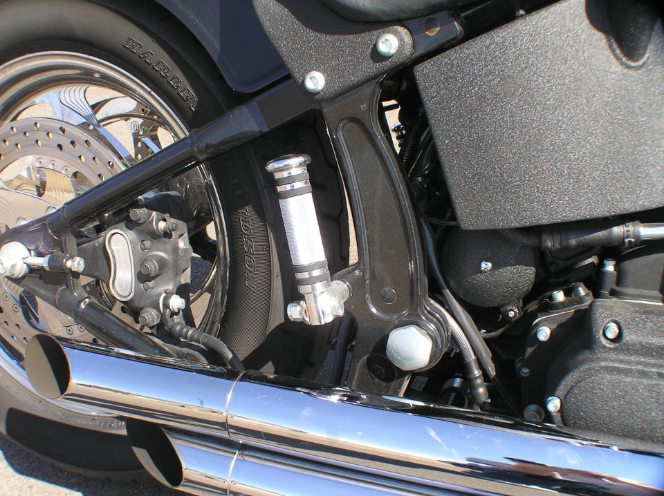 Close-up of black Harley Softail showing chrome exhaust, rear brake, footpeg and tire.