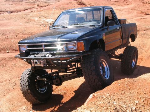 1986 Ford F-150 - This modified Toyota pickup truck features significant lift and oversized tires, suggesting it's built for off-road performance.