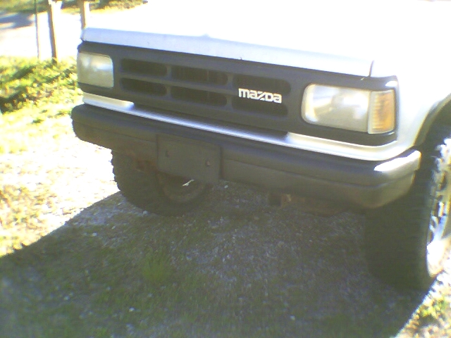 Front grille and bumper of a silver Mazda SUV with MAZDA lettering, parked on gravel