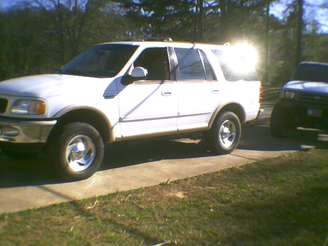 White four-door SUV parked on a concrete driveway, side view, with sun glare on rear window