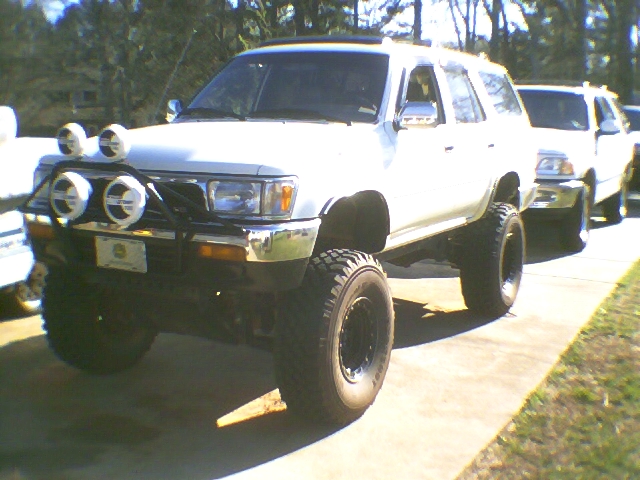 White lifted SUV with brush guard, four round lights, and large off-road tires in a driveway