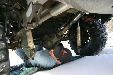 2003 Jeep TJ - A person works on the drivetrain of a vehicle, with snow on the ground and tires.