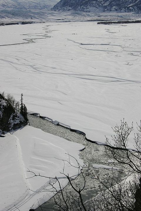2003 Jeep TJ - A vast, snow-covered landscape with a partially frozen river winding through it, under a muted sky.