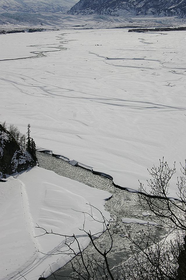 Frozen river with ice floes and snow-covered banks, distant mountains under a cloudy sky