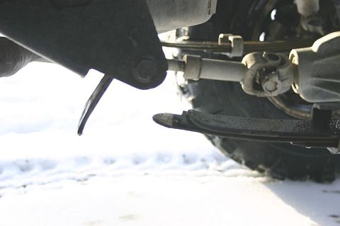 2003 Jeep TJ - Close-up view of the undercarriage, highlighting a bent leaf spring and driveshaft components in a snowy environment.