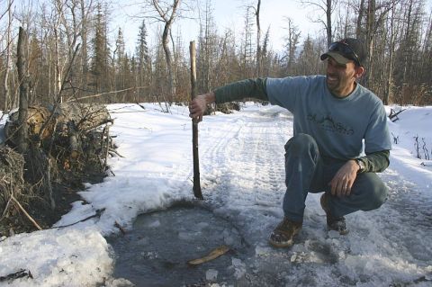 2003 Jeep TJ - Man in snowy woods points at ice on a track, with fallen trees in the background.