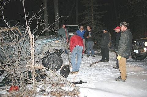 2003 Jeep TJ - A group of people gather around a green Jeep Wrangler in a snowy, wooded area at night.