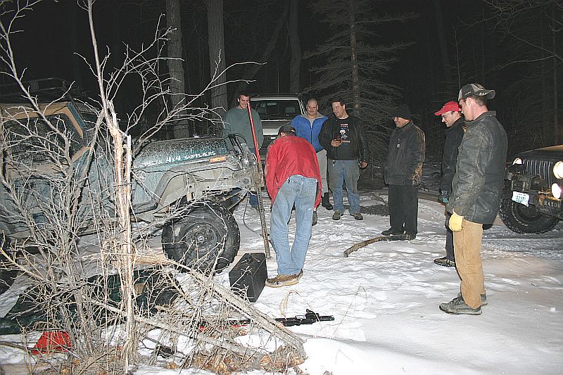 Green Jeep Wrangler with "4x4 SUPREME" text on fender, parked in snow with people around it