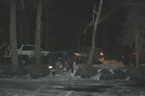 2003 Jeep TJ - Several off-road vehicles, including a black Jeep TJ, are parked in a wooded area at night with snow on the ground.