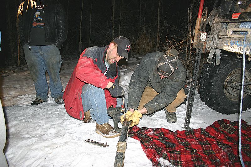 People working on a vehicle in the snow at night, with a winch visible