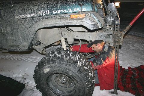 2003 Jeep TJ - A person uses a Hi-Lift jack to lift a muddy Jeep in a snowy environment.
