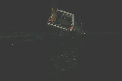 2003 Jeep TJ - A white SUV is partially submerged in dark water, with its rear hatch open and a person visible inside.