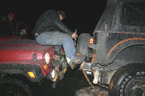 2003 Jeep TJ - A man sits on the hood of a red Jeep TJ as it is positioned next to a black off-road vehicle, likely during a recovery operation.