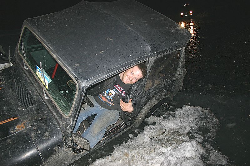 Man in a black 2003 Jeep TJ stuck in snow, driver's side door open
