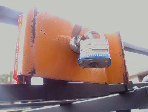 1993 Ford Bronco - A Master lock secures an orange accessory, possibly a tool holder, on a vehicle's roof rack.