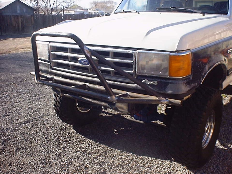 Front of a white and dark blue Ford truck with a custom metal bumper and 4x4 decal