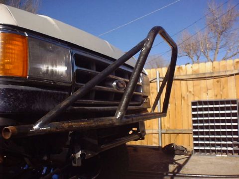 1988 Ford Bronco - Low-angle view of a bare steel tube front bumper with a tall welded brush-guard hoop and diagonal gussets mounted to a white Ford truck, tu…